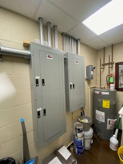 Finished interior panel room with multiple labeled panels mounted side by side, conduit cleanly run between them