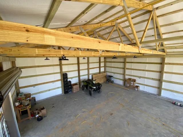 Wide interior view of the shop with vaulted wood-truss ceiling, UFO LED high bays mounted, ATV parked in the work area