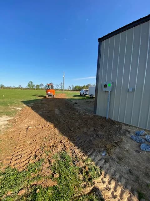 Mini-excavator working a service trench out to the shop on a clear day